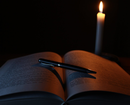 black pen on opened book beside lit taper candle