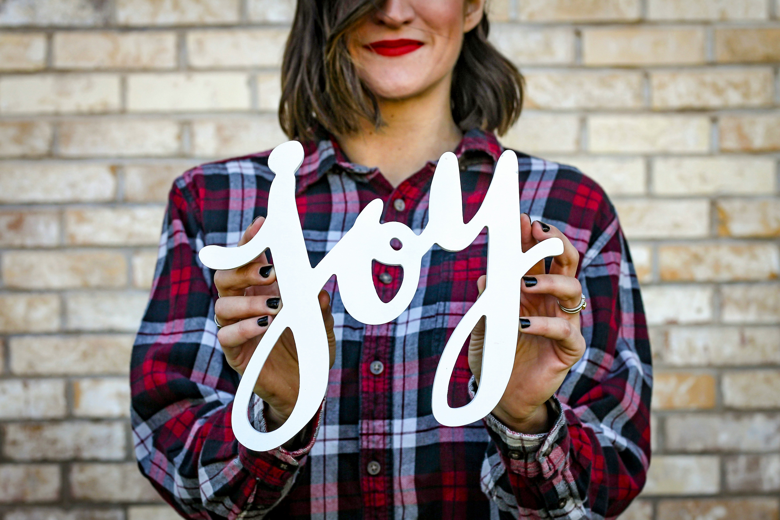 Woman in blue and red plaid shirt holding a sign saying joy in cursive letters.