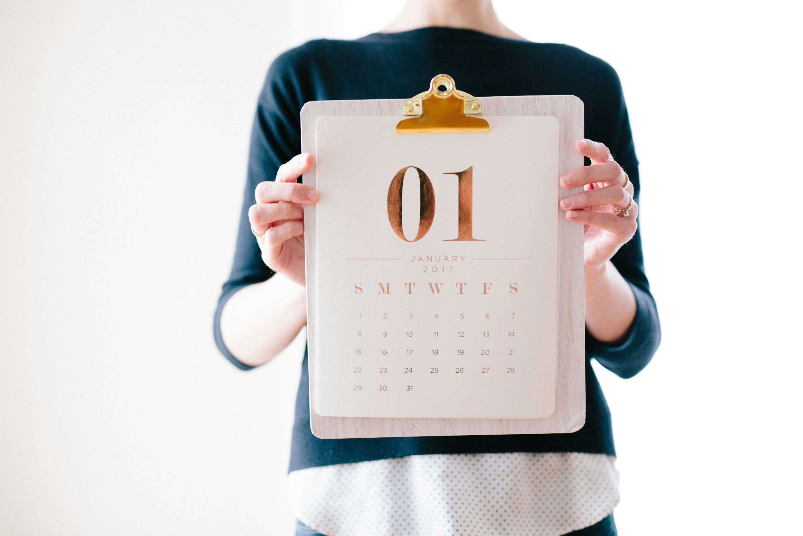 Faceless woman in blue shirt holding a January calendar on a clipboard in front of her chest.